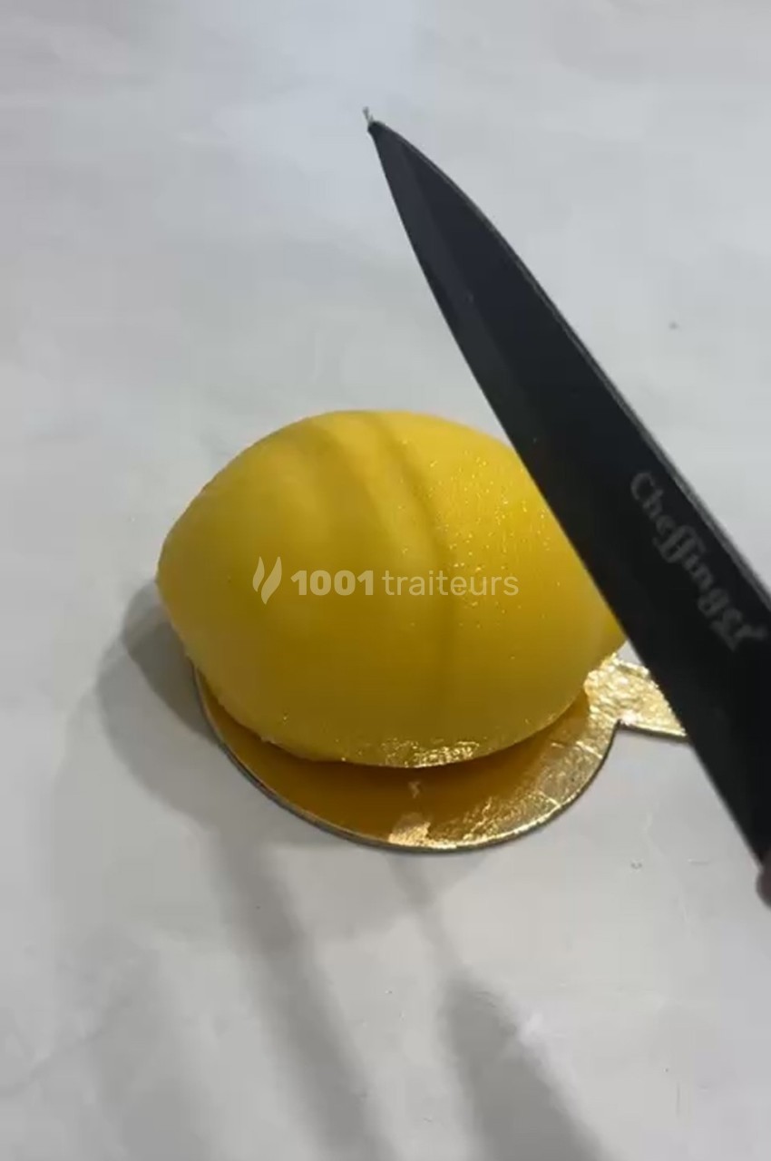 Un couteau s'apprête à couper un dessert en forme de citron jaune posé sur un support doré.