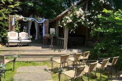 Salle lumineuse avec une grande table blanche, un vase de fleurs vertes et des chaises en bois devant des baies vitrées.