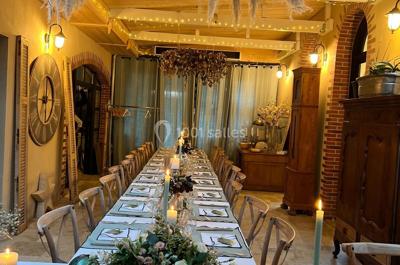 Grande table décorée pour un dîner, avec chandeliers, fleurs et guirlandes lumineuses dans une salle chaleureuse.