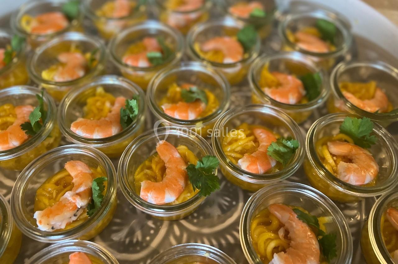 Verrines de crevettes sur lit de pâtes et sauce jaune, décorées de feuilles de coriandre.