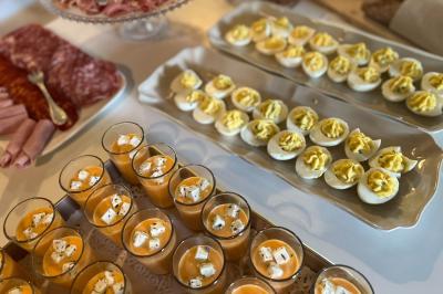 Salle lumineuse avec une grande table blanche, un vase de fleurs vertes et des chaises en bois devant des baies vitrées.