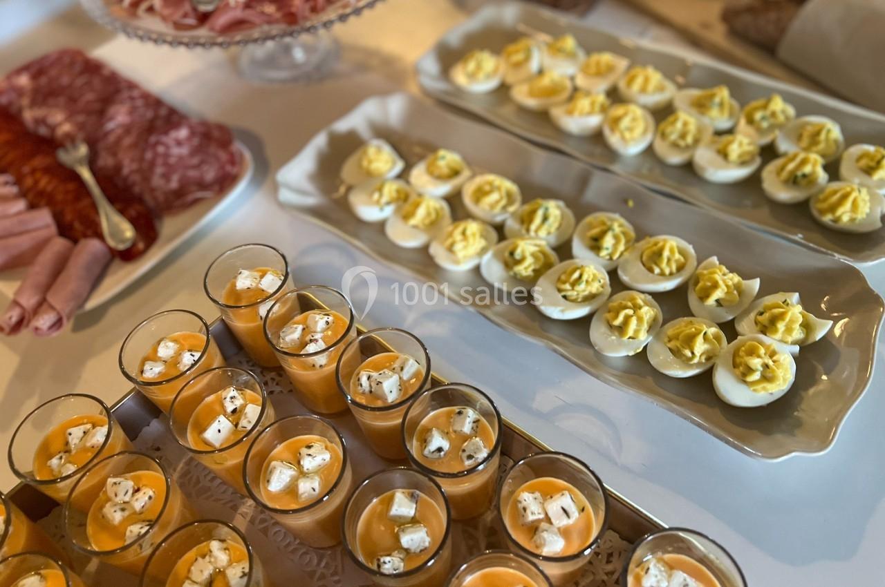 Plateau de charcuterie, œufs mimosa et verrines de soupe froide garnies de fromage sur une table de buffet.