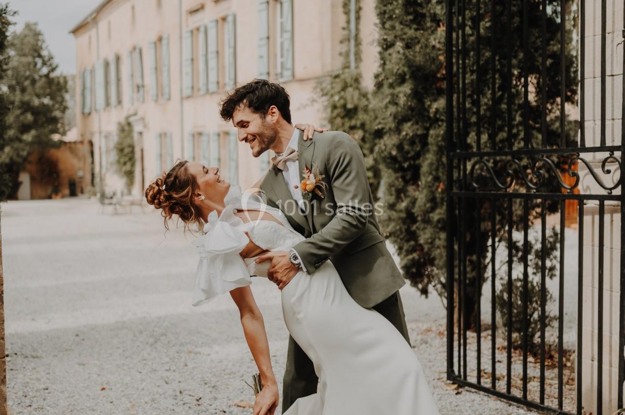 Un couple en tenue de mariage danse devant un bâtiment ancien entouré de végétation.