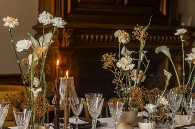 Salle lumineuse avec poutres apparentes, tables blanches disposées en U et chaises rouges, éclairée par des lustres et des…