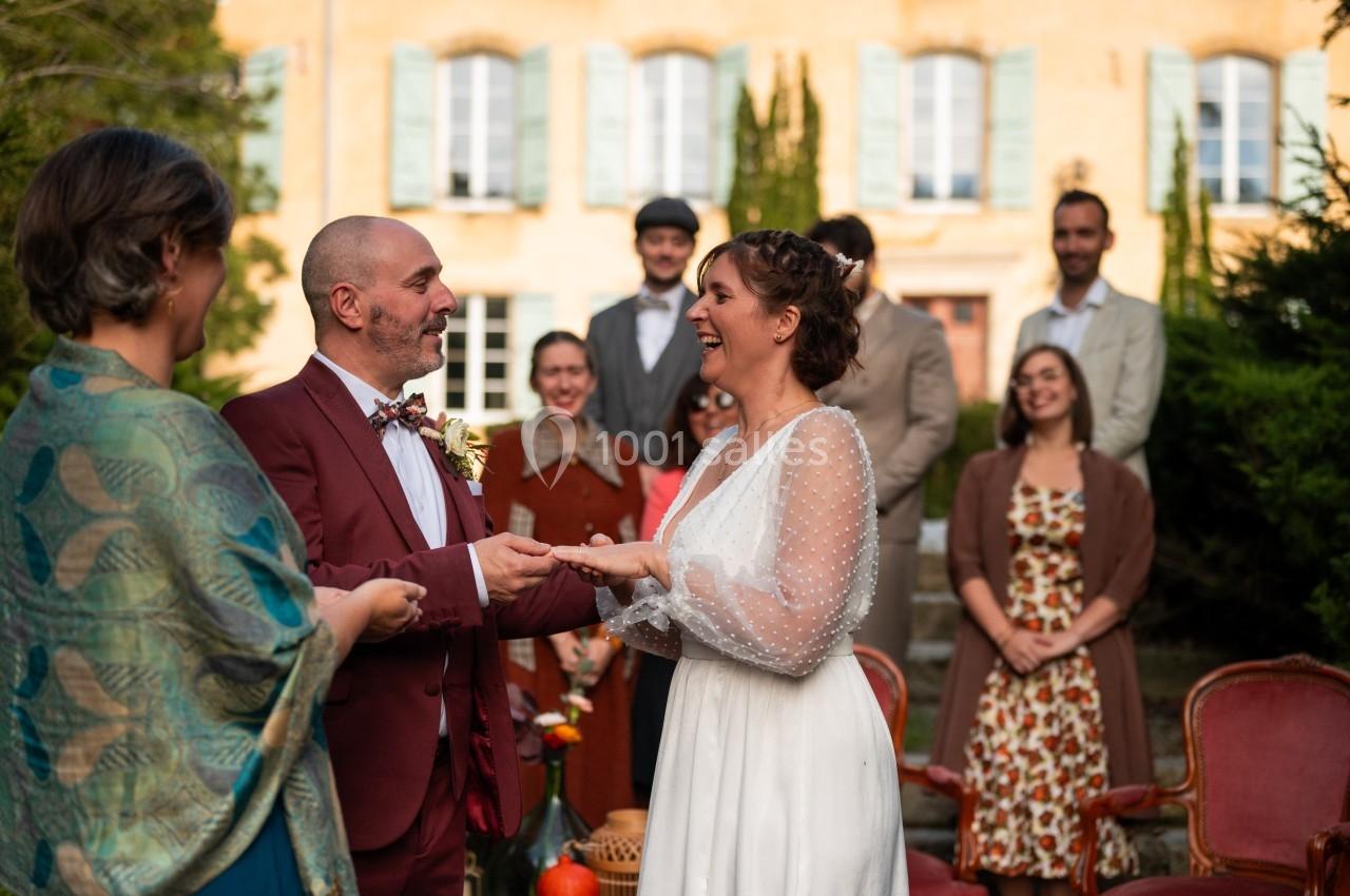 Un couple échange ses vœux lors d'une cérémonie de mariage en extérieur, entouré de leurs proches souriants.