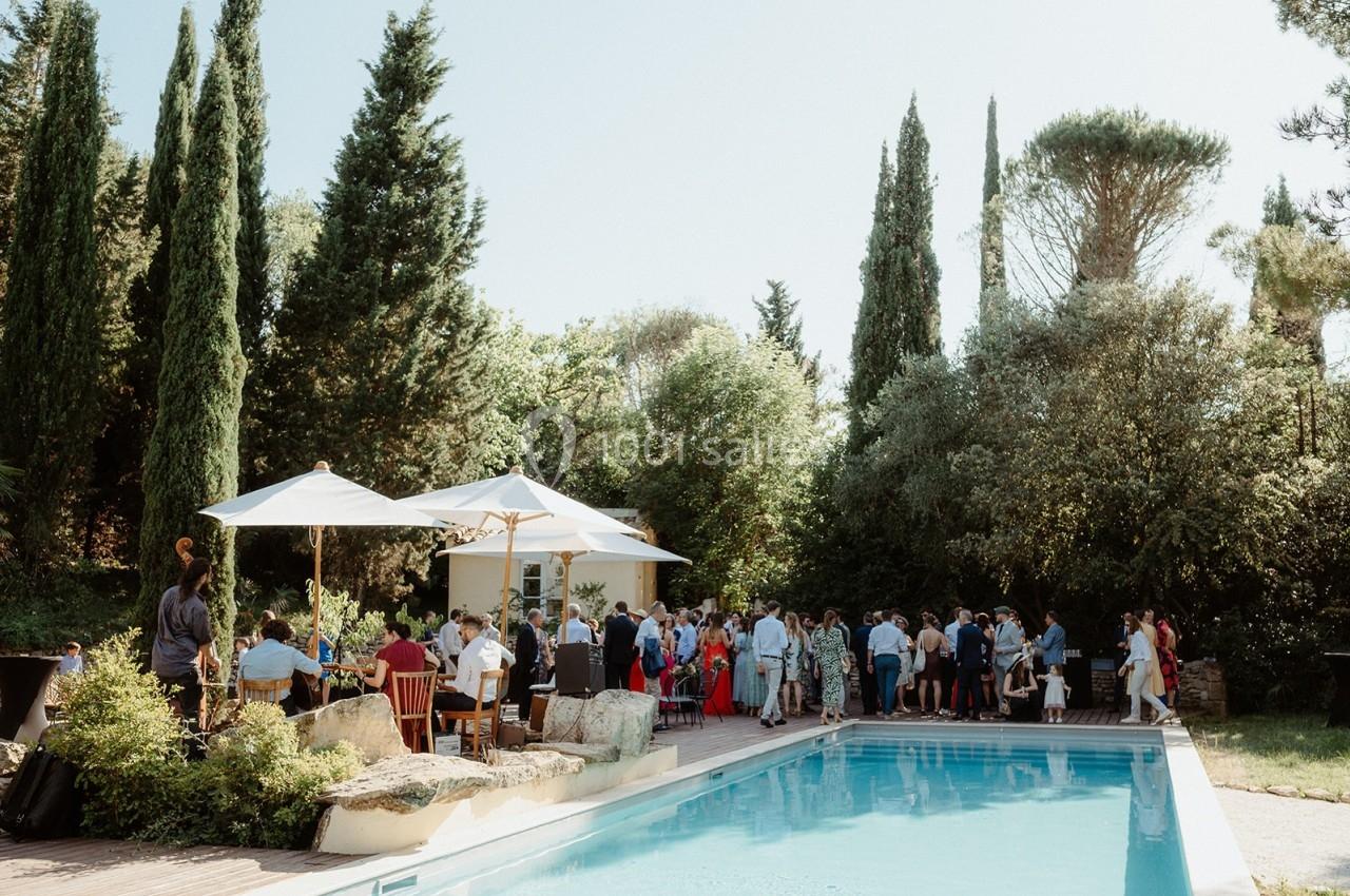 Groupe de personnes réunies près d'une piscine entourée de végétation et de parasols sous un ciel dégagé.