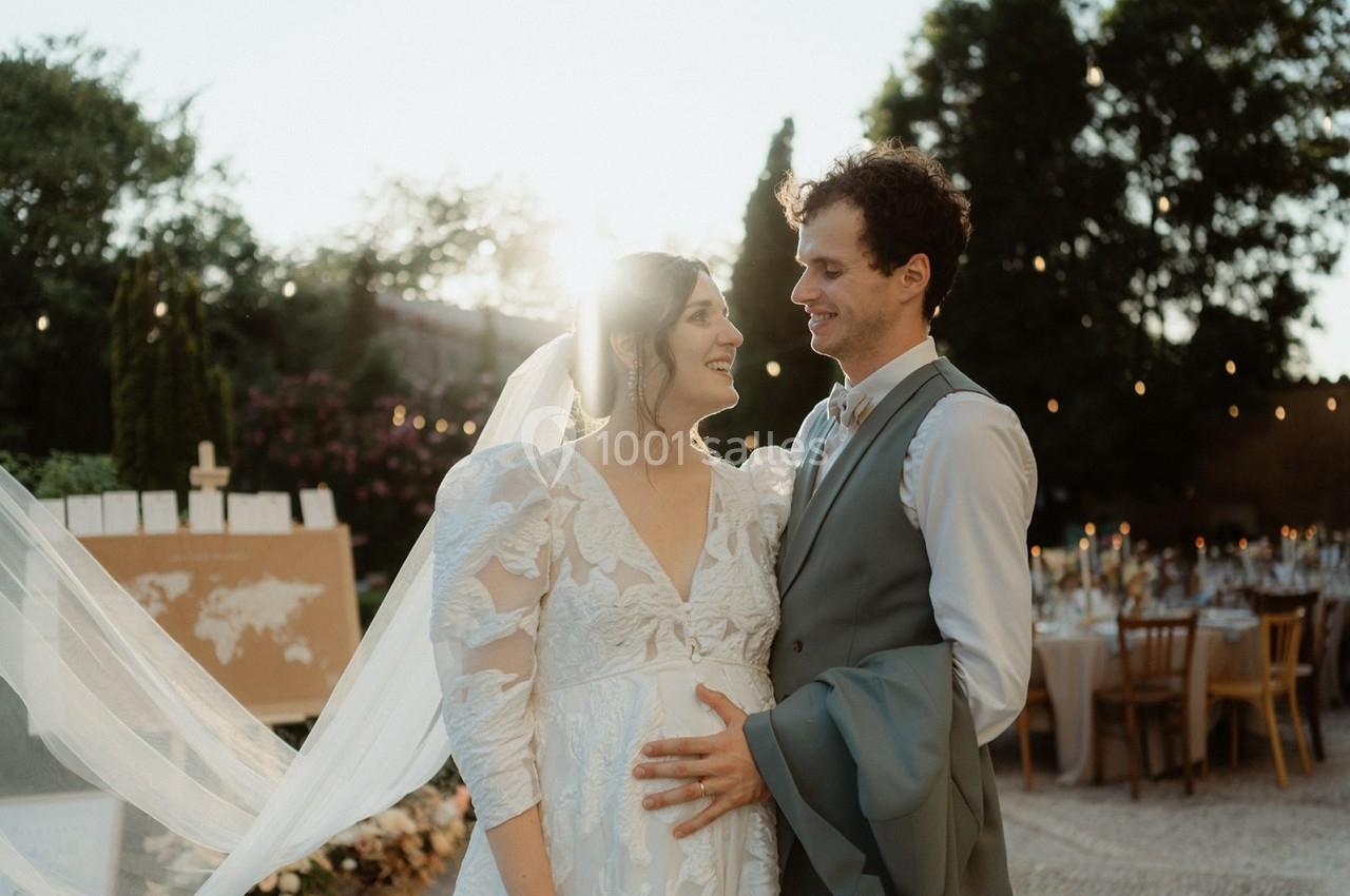 Un couple en tenue de mariage se tient dans un jardin décoré, éclairé par une lumière douce au coucher du soleil.