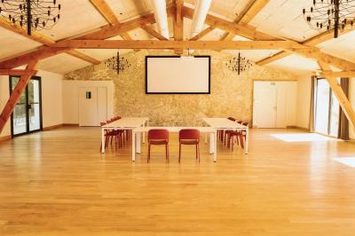 Salle lumineuse avec poutres apparentes, tables blanches disposées en U et chaises rouges, éclairée par des lustres et des…