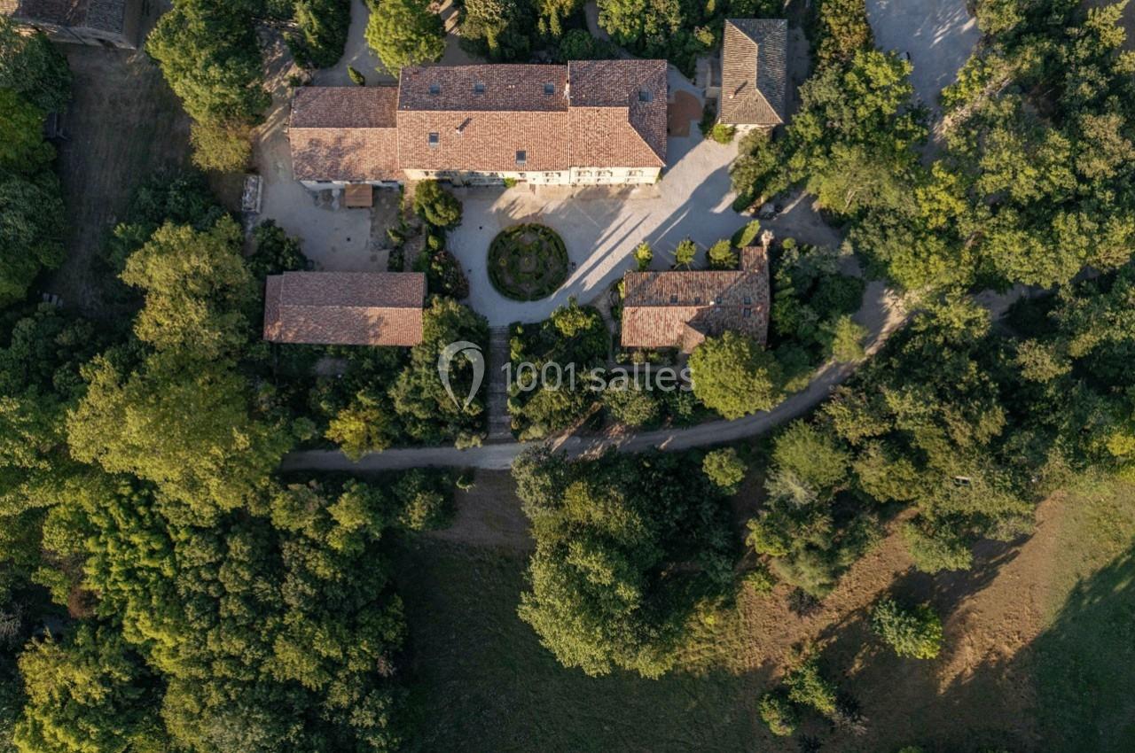 Vue aérienne d'un domaine rural entouré de végétation, avec plusieurs bâtiments en pierre et une cour centrale.