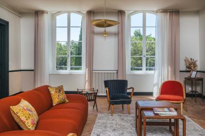 Salle lumineuse avec poutres apparentes, tables blanches disposées en U et chaises rouges, éclairée par des lustres et des…