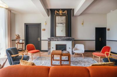 Salle lumineuse avec poutres apparentes, tables blanches disposées en U et chaises rouges, éclairée par des lustres et des…
