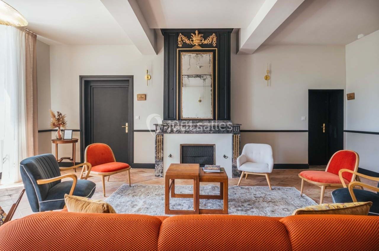 Salon lumineux avec cheminée, miroir doré, fauteuils colorés et table basse sur un tapis clair.