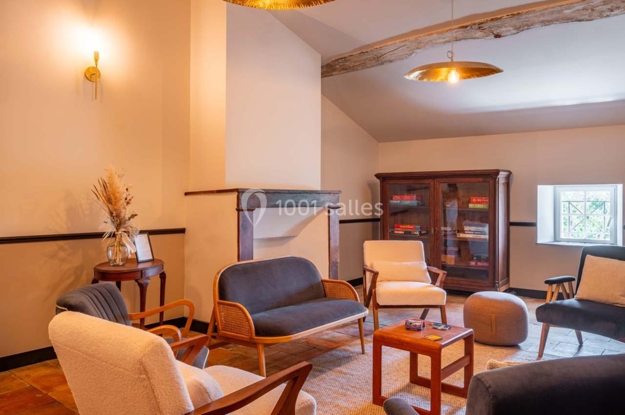 Espace de détente avec fauteuils, table basse, bibliothèque vitrée et lumière naturelle dans une pièce chaleureuse.