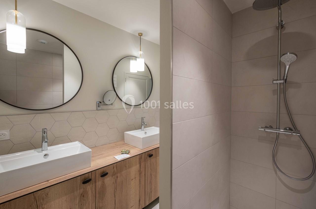 Salle de bain moderne avec deux lavabos, miroirs ronds, meuble en bois et douche à l'italienne carrelée.