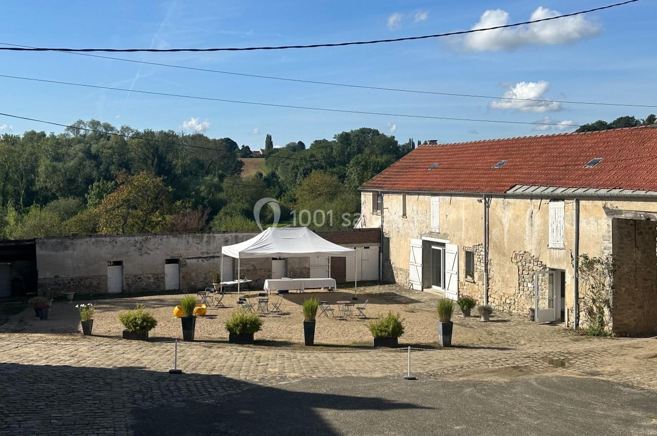 Cour d'une ferme rénovée avec des bâtiments en pierre, une tente blanche et des tables installées, entourée de verdure.