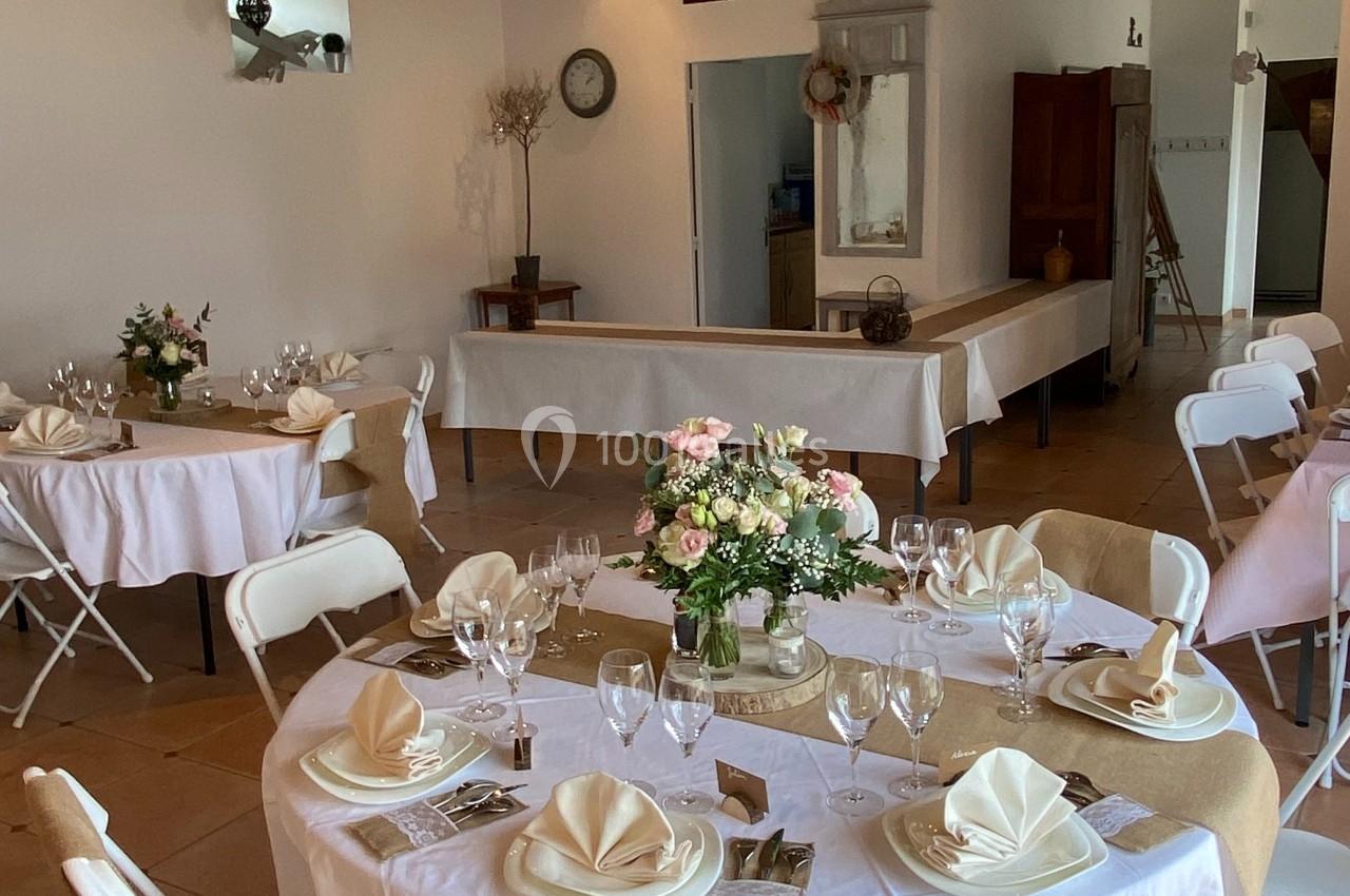 Salle décorée pour un événement avec tables rondes dressées, nappes blanches, serviettes pliées et compositions florales.