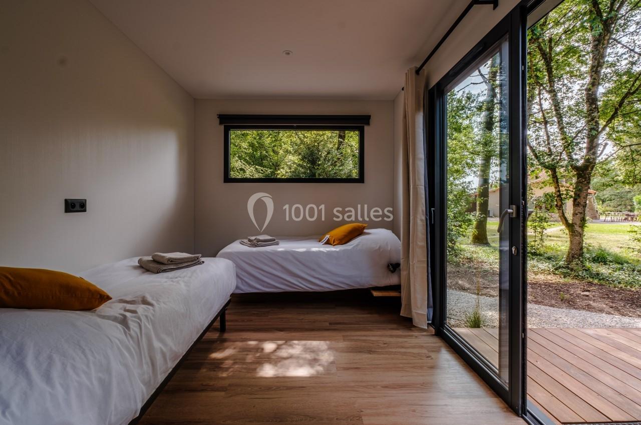 Deux lits simples avec coussins jaunes dans une chambre lumineuse, vue sur un jardin à travers une baie vitrée.