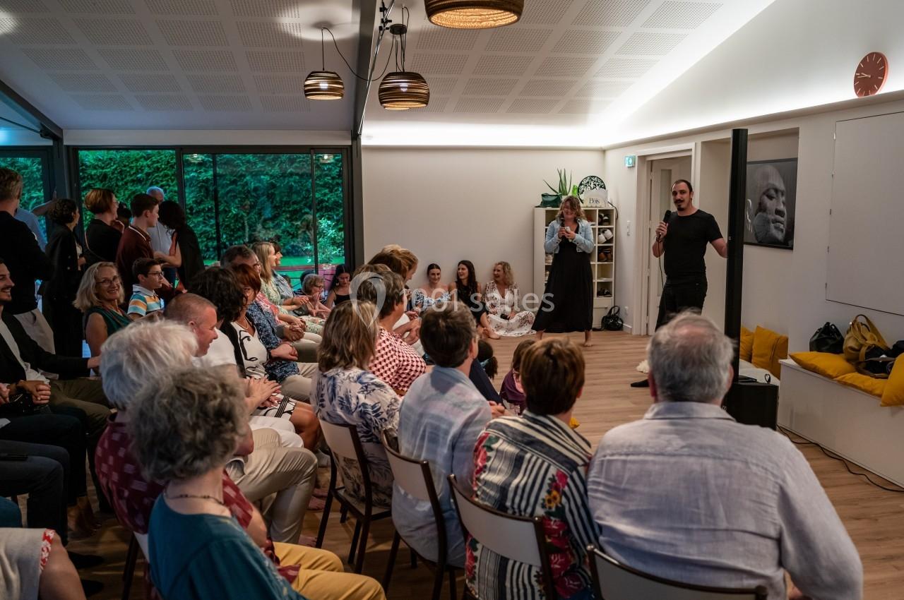 Un homme s'exprime devant un public assis dans une salle lumineuse avec des décorations modernes.