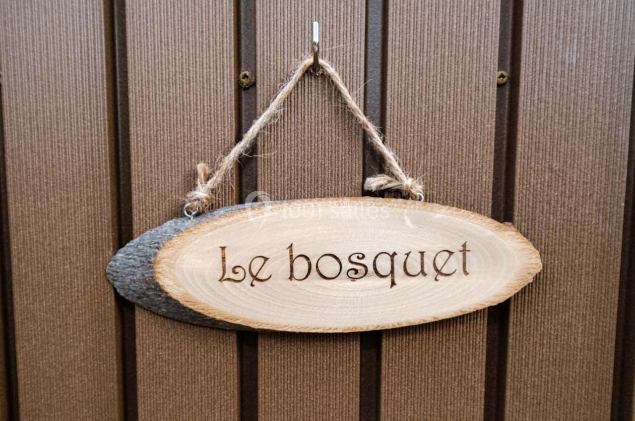 Pancarte en bois suspendue avec l'inscription ’Le bosquet’, accrochée sur un mur en bois brun.