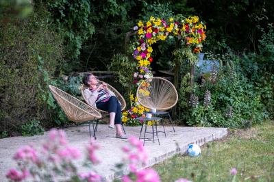 Jardin verdoyant avec fleurs sauvages, arbres et arbustes, entouré d'une clôture en bois sous un ciel dégagé.