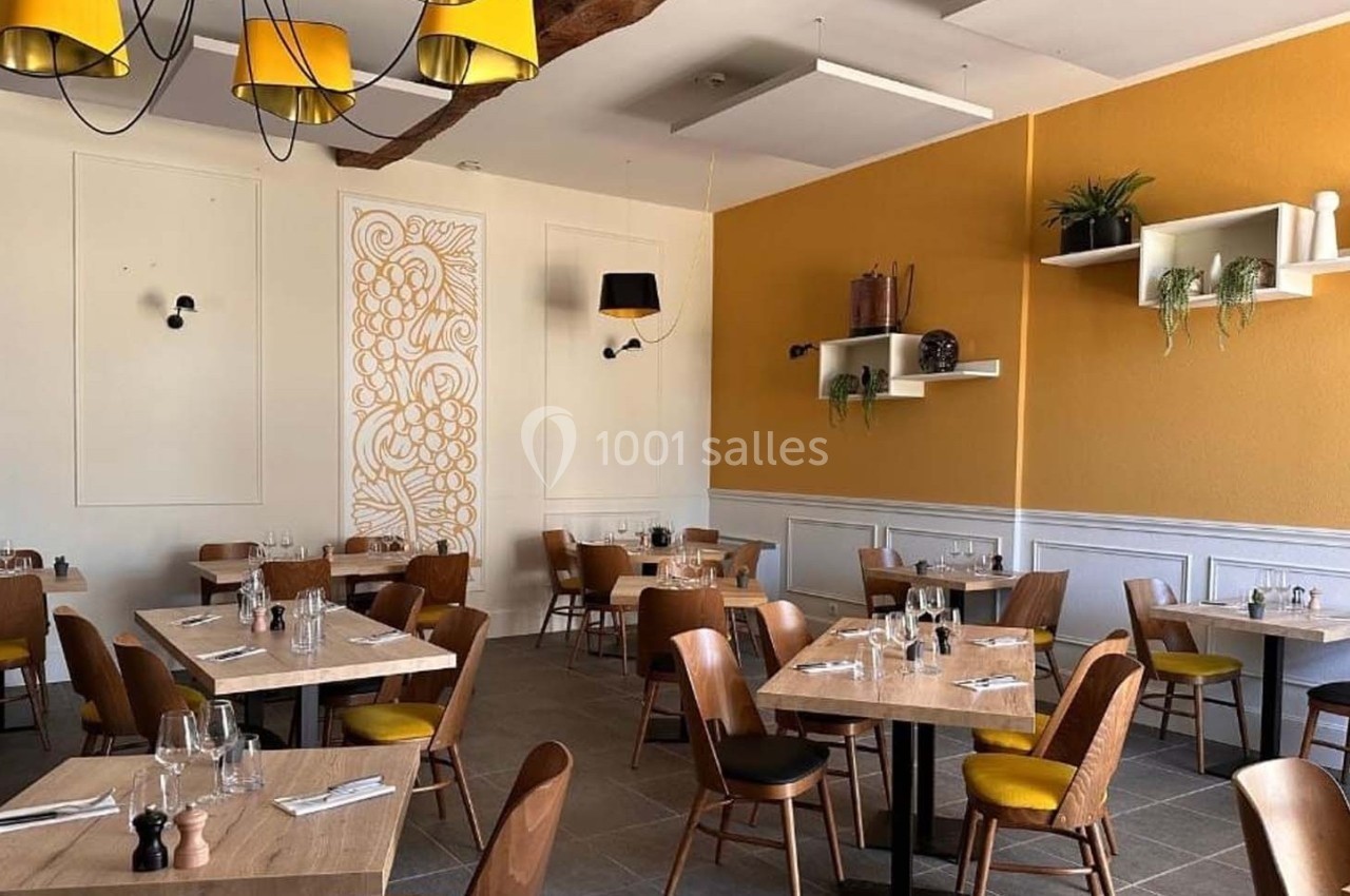 Salle de restaurant lumineuse avec tables en bois, chaises jaunes, décoration murale et étagères avec plantes.