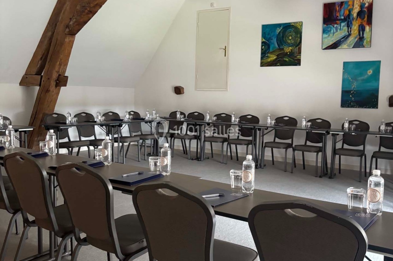 Salle de réunion lumineuse avec des tables en U, des chaises, des bouteilles d'eau et des tableaux accrochés aux murs.