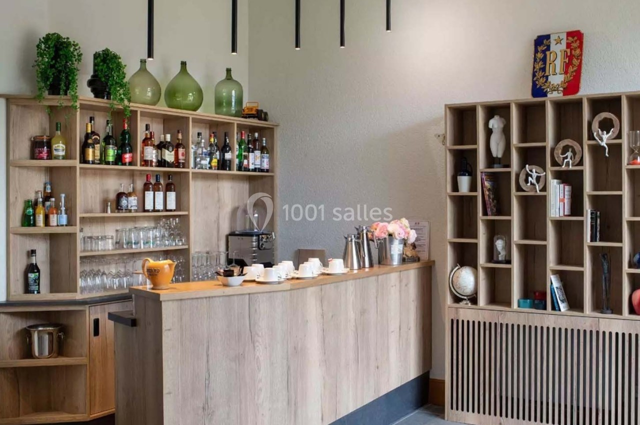 Comptoir en bois avec étagères contenant des bouteilles, tasses, objets décoratifs et plantes dans un espace lumineux.