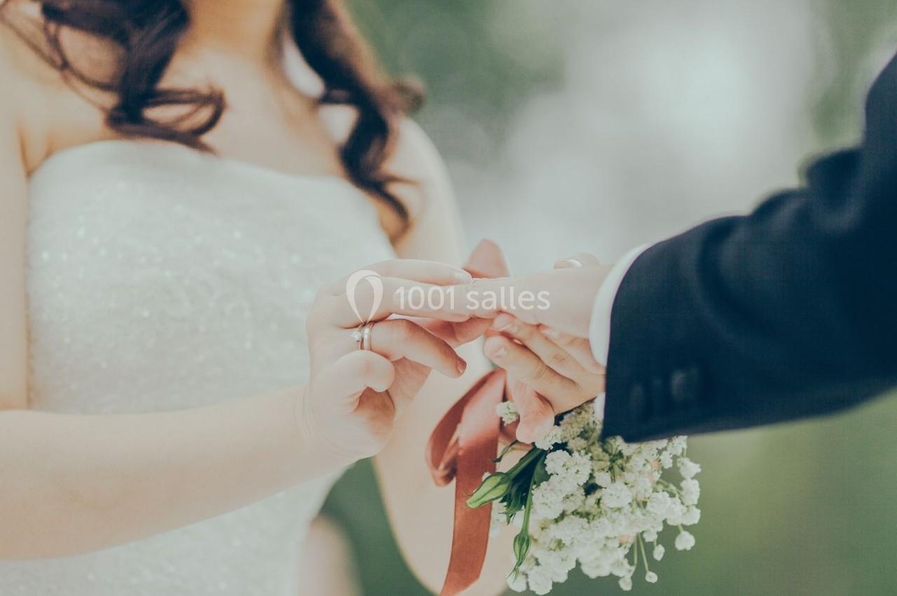 Une mariée en robe blanche passe une alliance au doigt de son partenaire, tenant un bouquet de fleurs blanches.