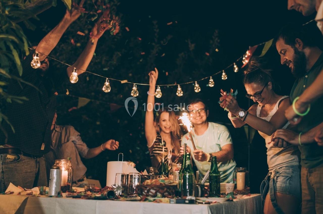 Groupe de personnes célébrant autour d'une table décorée, avec guirlandes lumineuses et ambiance festive en soirée.