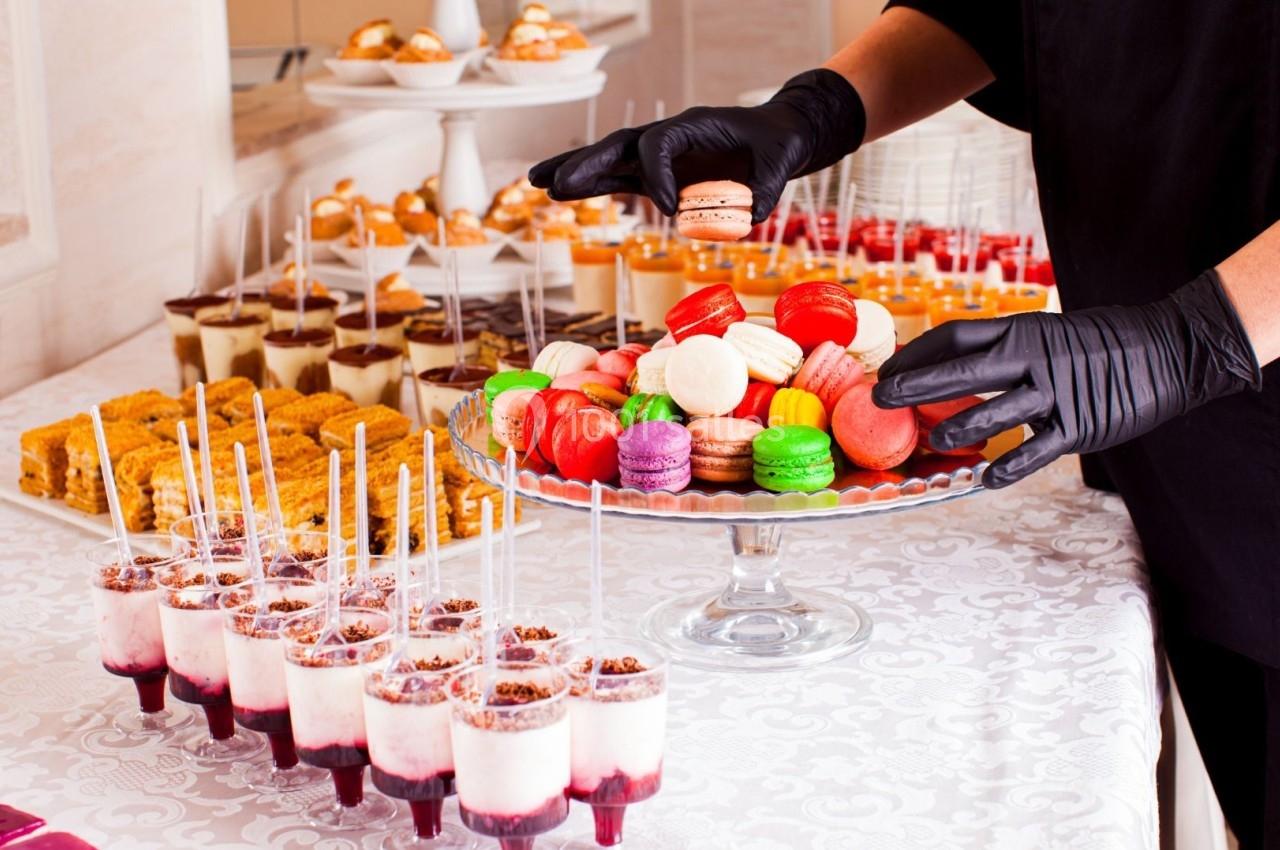 Une personne dispose des macarons colorés sur un plateau au milieu d'un buffet de desserts variés.