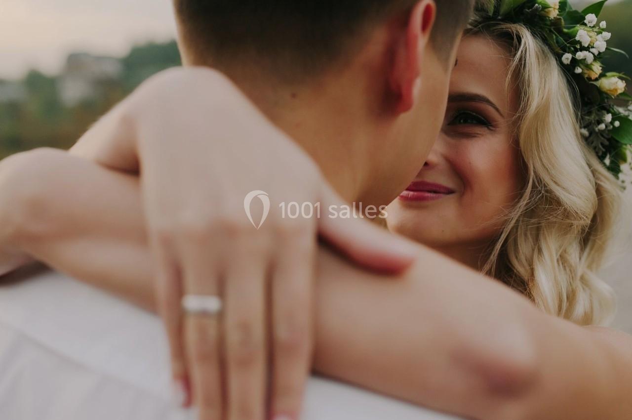 Une femme souriante portant une couronne de fleurs enlace un homme, vue rapprochée dans un cadre extérieur flou.
