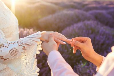 Un couple marche dans un champ au coucher du soleil, la femme portant une robe blanche et tenant légèrement son ourlet.