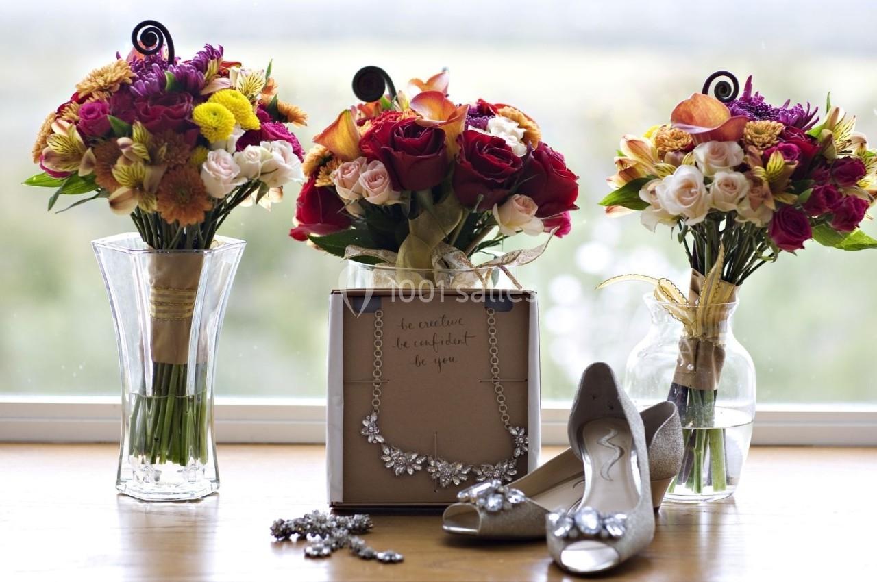Trois bouquets de fleurs colorées, un coffret de bijoux et des chaussures ornées posés sur une table en bois.