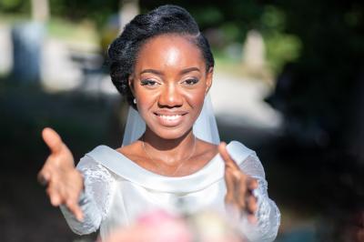 Femme en robe blanche souriante, assise près d'une fontaine, avec un homme en costume visible de dos.