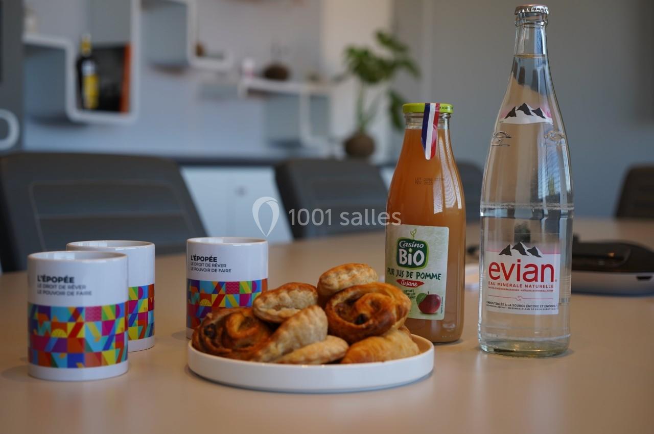 Assortiment de viennoiseries sur une table avec des tasses, une bouteille de jus de pomme et une bouteille d'eau minérale.