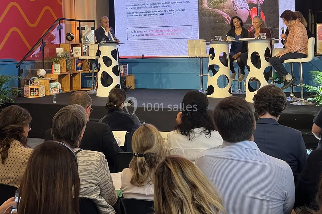 Un panel de quatre intervenants discute sur une scène devant un public, avec une présentation projetée en arrière-plan.