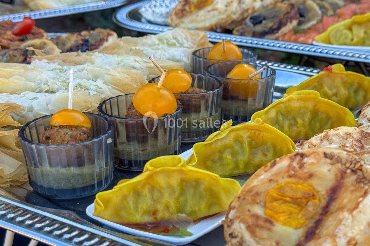 Assortiment de bouchées salées comprenant raviolis, feuilletés, boulettes et légumes, présentés sur des plateaux.