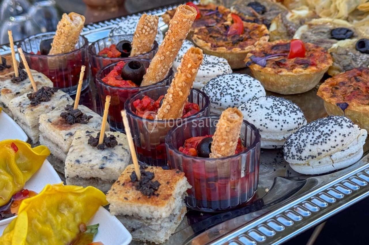 Plateau de bouchées apéritives variées comprenant verrines, mini-tartes, pains garnis et raviolis colorés.