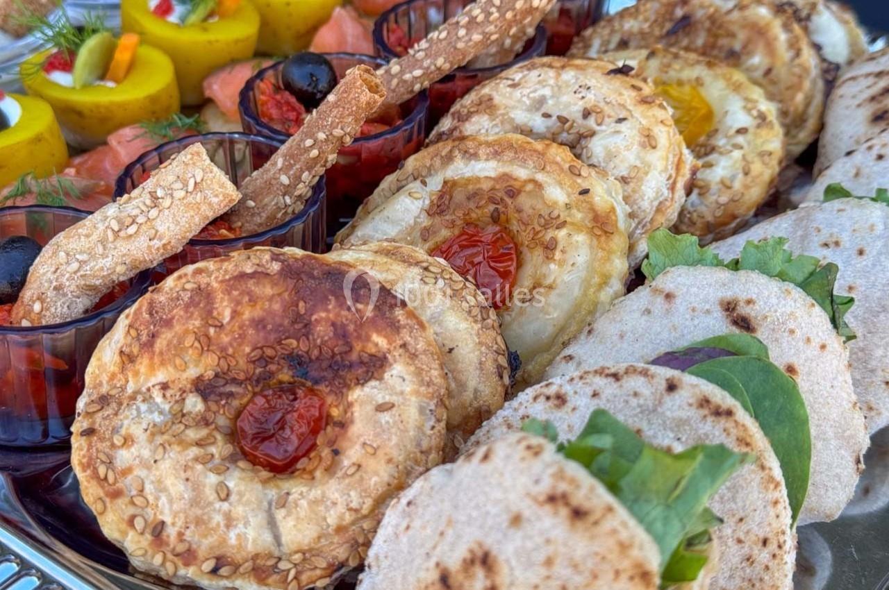 Plateau de bouchées variées comprenant feuilletés, wraps garnis, roulés de saumon et verrines colorées.
