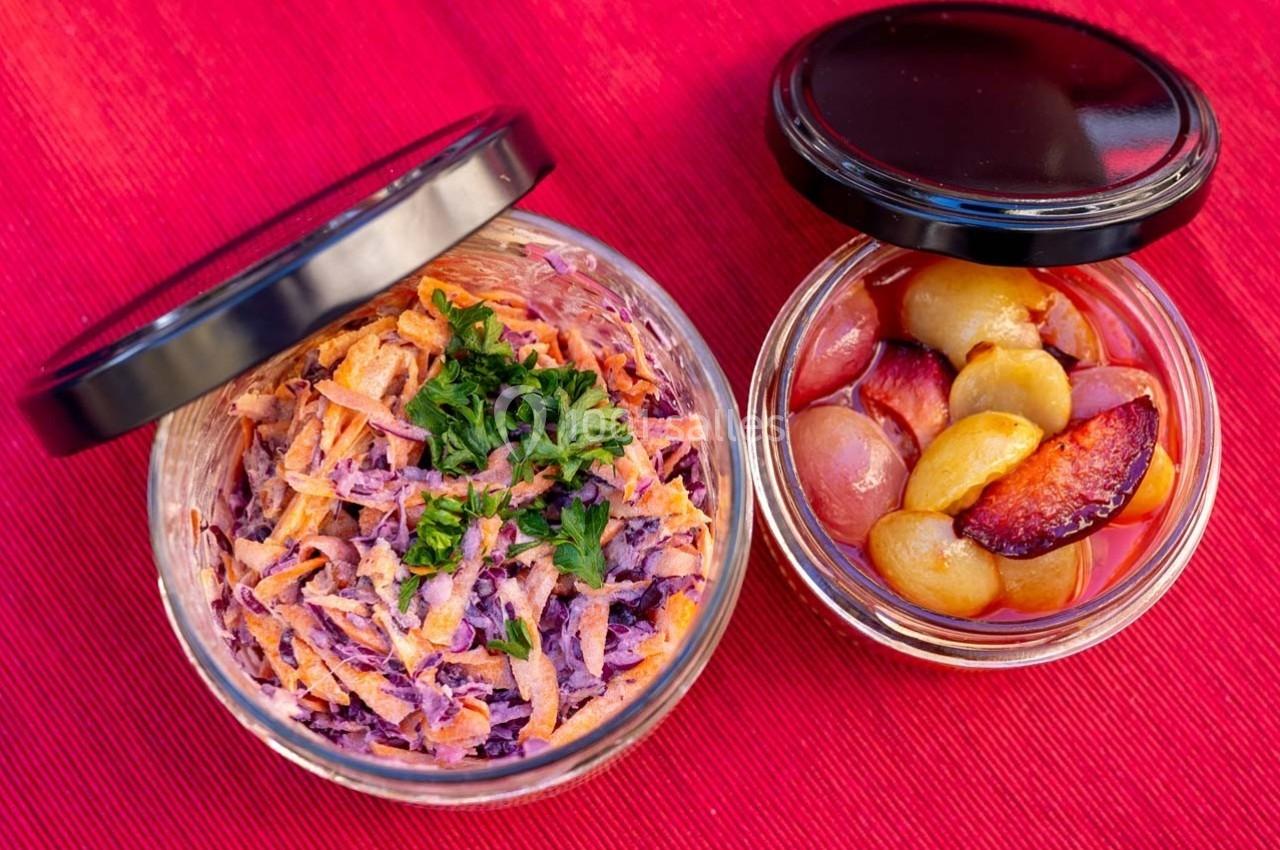 Deux bocaux ouverts contenant une salade de carottes et chou rouge garnie de persil, et des fruits marinés.