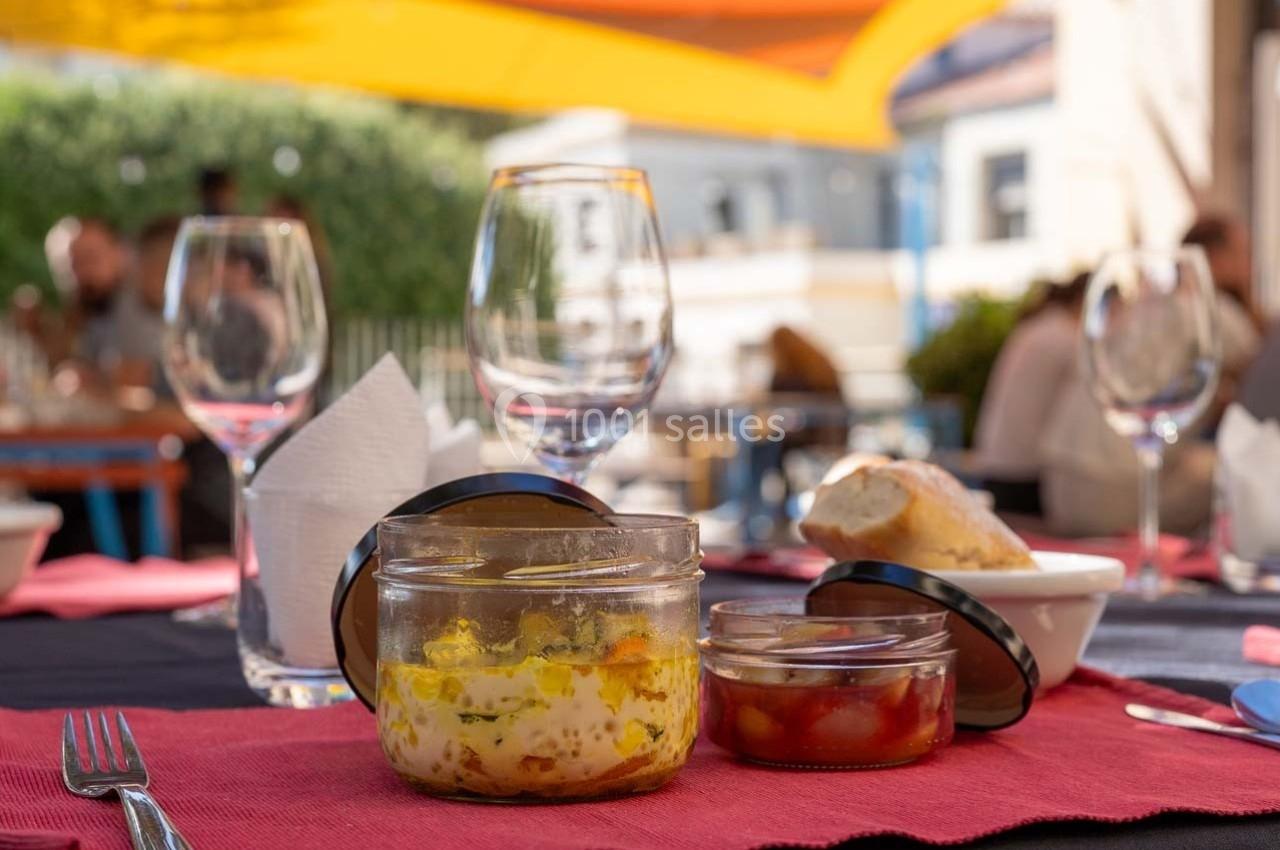 Repas en terrasse avec des verrines, du pain et des verres vides sur une table dressée avec des nappes colorées.