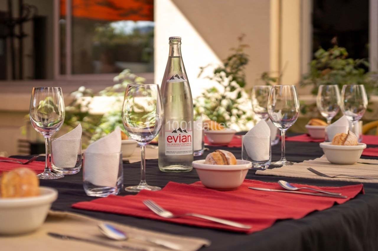 Table dressée avec nappes colorées, verres, couverts, serviettes et une bouteille d'eau au centre, en extérieur.