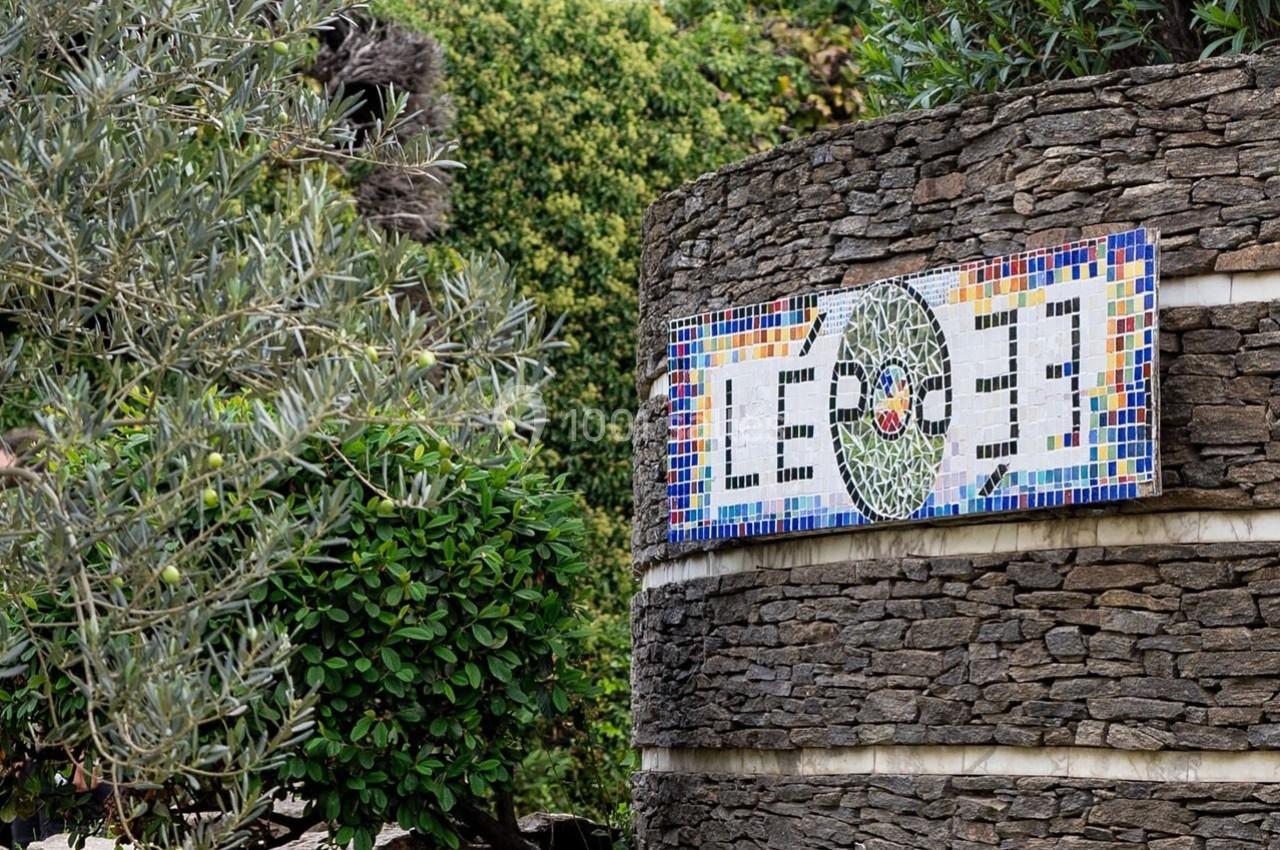 Mur en pierre orné d'une mosaïque colorée représentant un motif circulaire, entouré de végétation.
