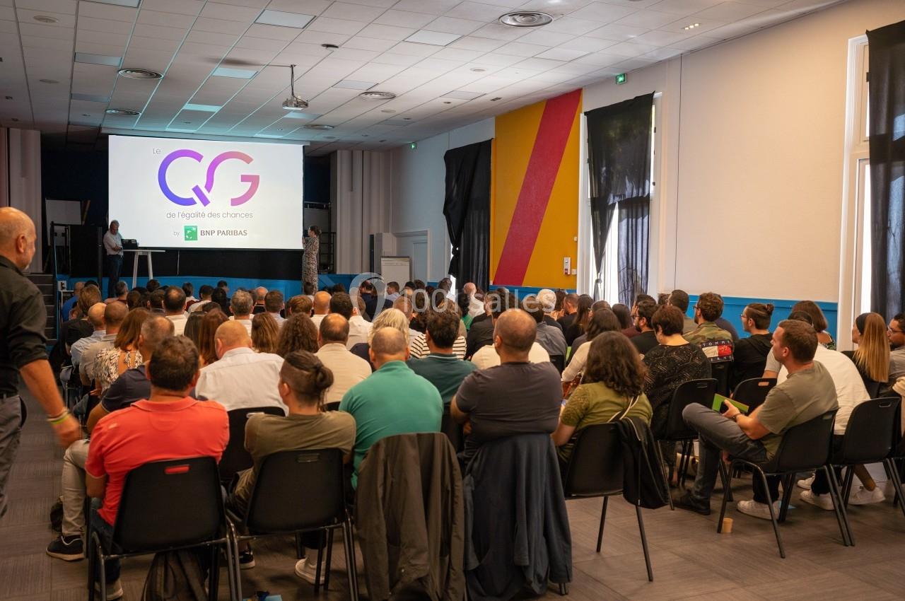 Salle de conférence avec un public attentif regardant une présentation projetée sur un écran.