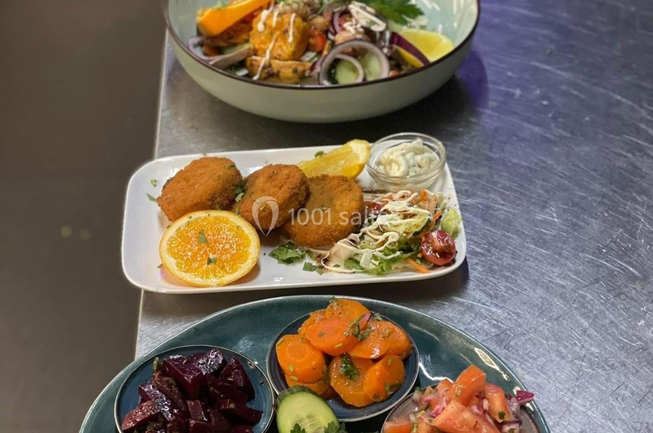 Assiette de falafels avec crudités et sauces, accompagnée de salades colorées sur une table en inox.