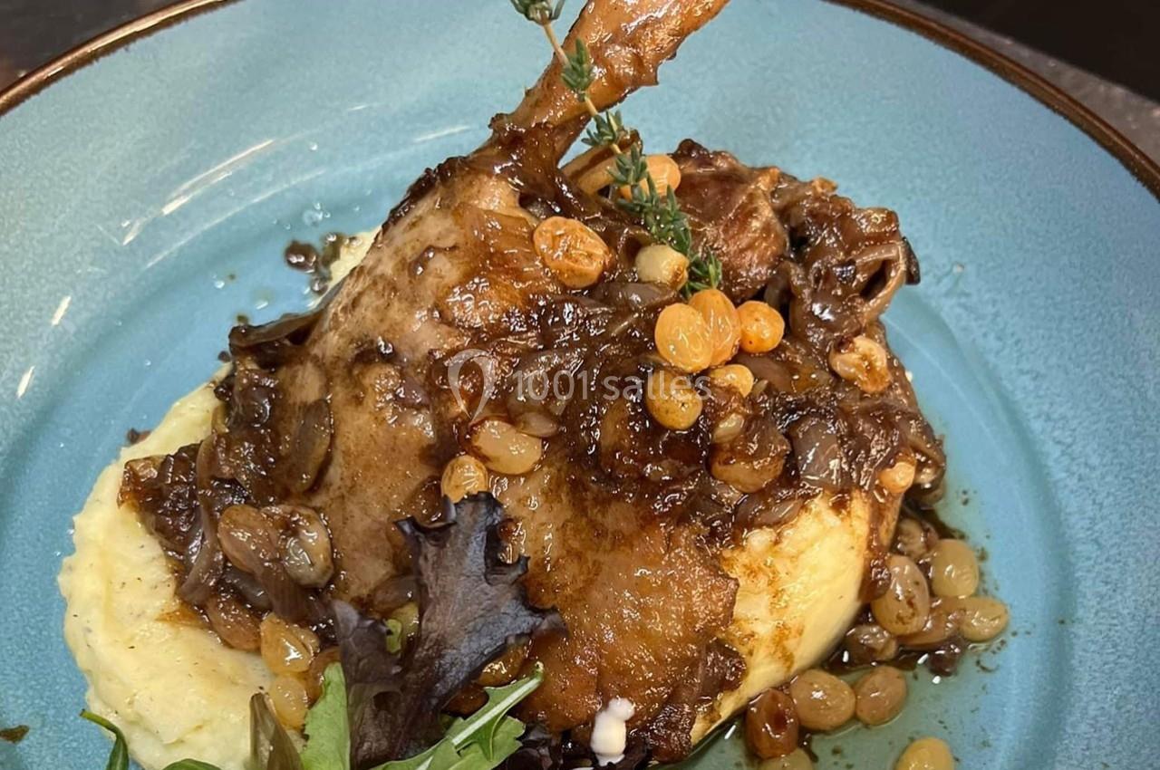 Plat de cuisse de volaille confite servie sur purée, nappée de sauce aux raisins secs et garnie de feuilles de salade.