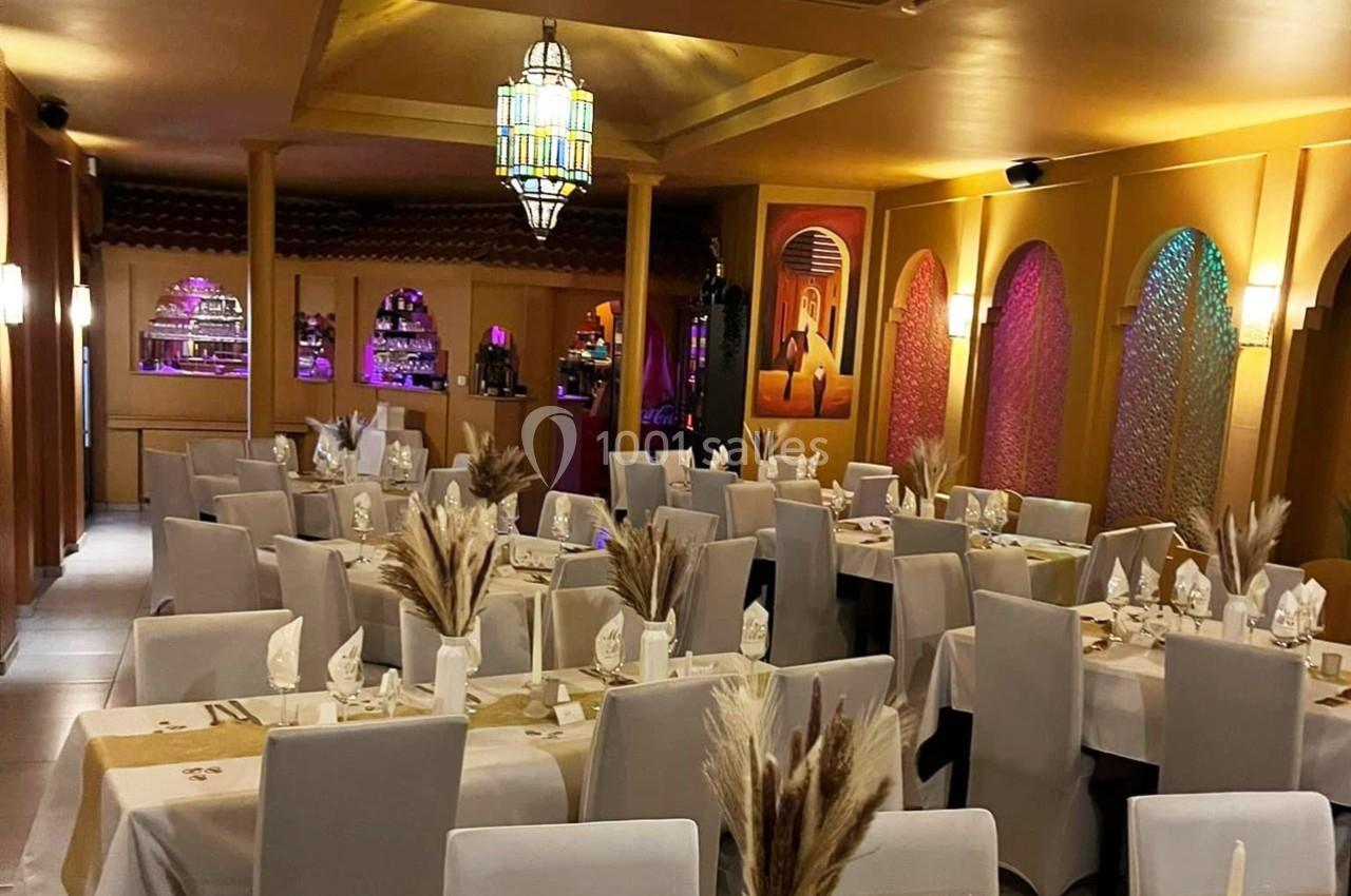 Salle de restaurant décorée dans un style oriental, avec tables dressées, chaises blanches et éclairage chaleureux.