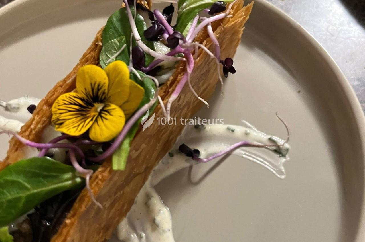 Feuilleté garni de légumes verts, pousses et fleur comestible, servi sur une sauce blanche parsemée d'herbes.
