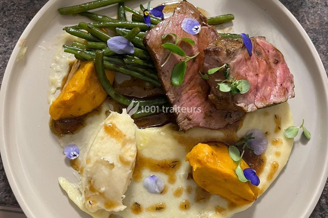 Assiette garnie de viande rosée, haricots verts, purées de pommes de terre et de patate douce, décorée de fleurs comestibles.