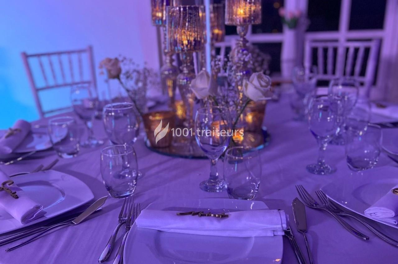 Table élégamment dressée avec vaisselle, bougies dorées et décorations florales dans une ambiance lumineuse tamisée.